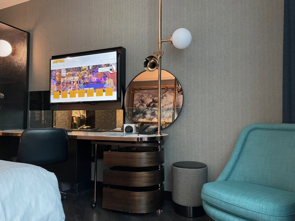 television, blue chair, mirror and executive desk in a hotel room
