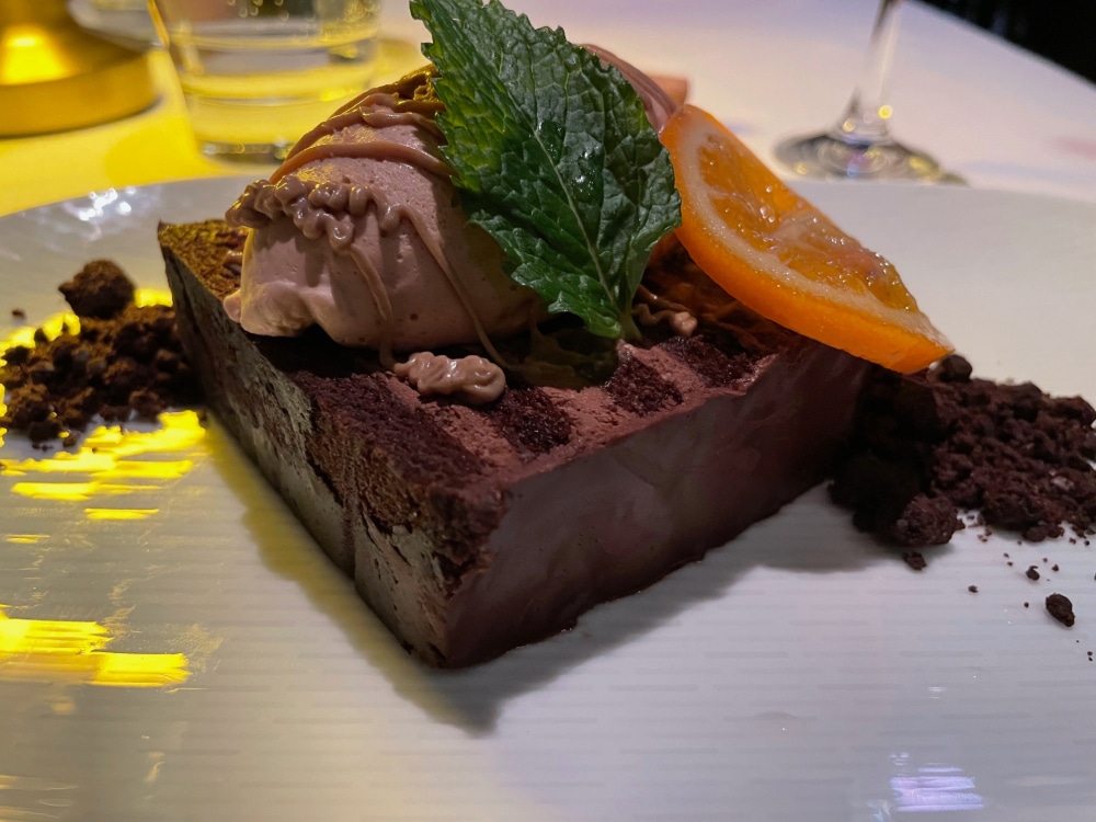 a slice of chocolate cake garnished with an orange slice and sprig of mint