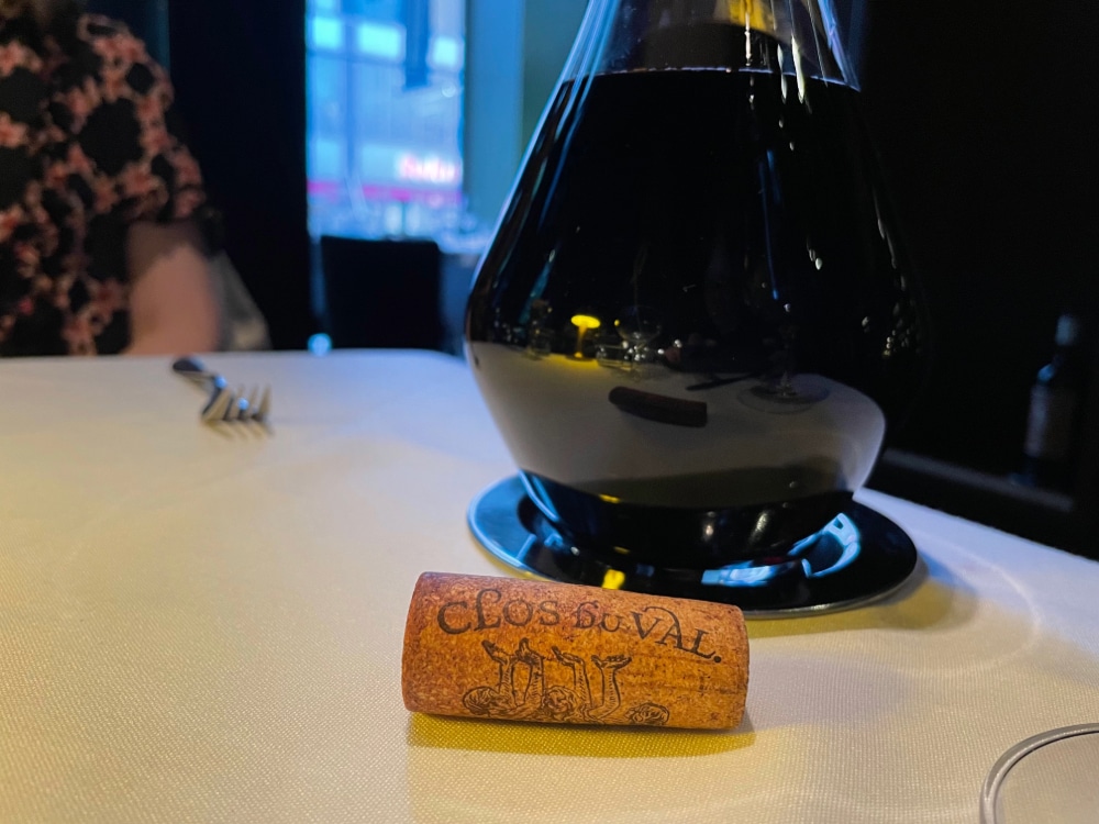 a decanter of red wine beside a wine cork