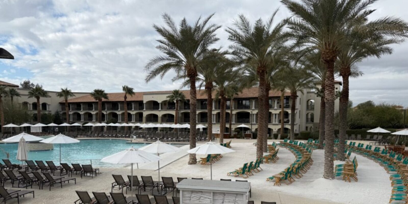 a pool at a resort with a white sand beach and palm trees