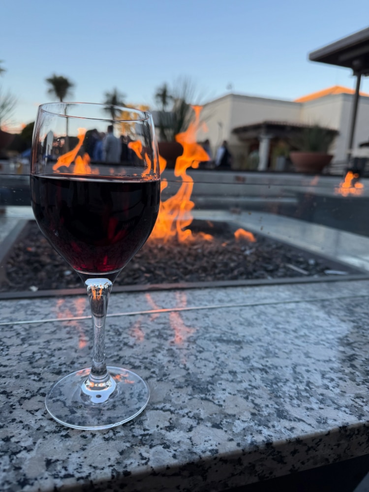 glass of wine sitting on the ledge of a fire table