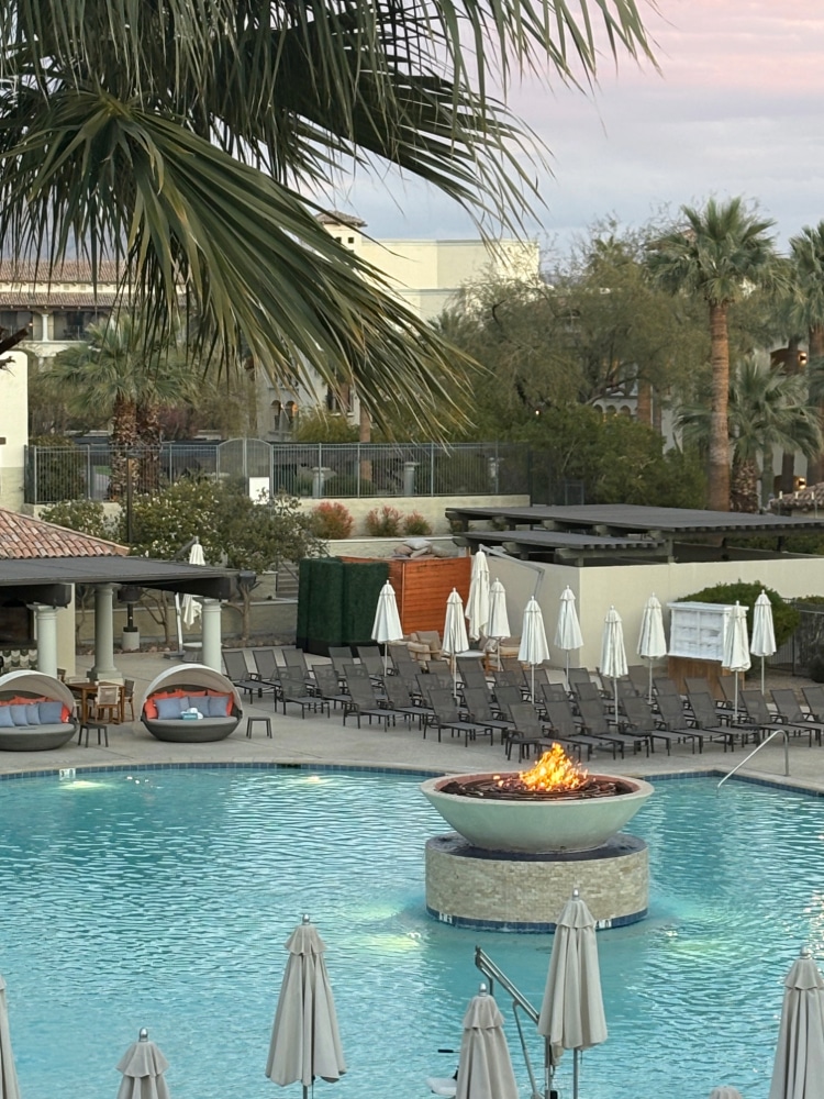 outdoor resort pool flanked by palm trees with a lit fire feature in the centre