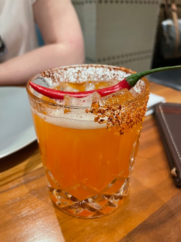 a margarita topped with a red chili pepper and rimmed with hot pepper flake salt
