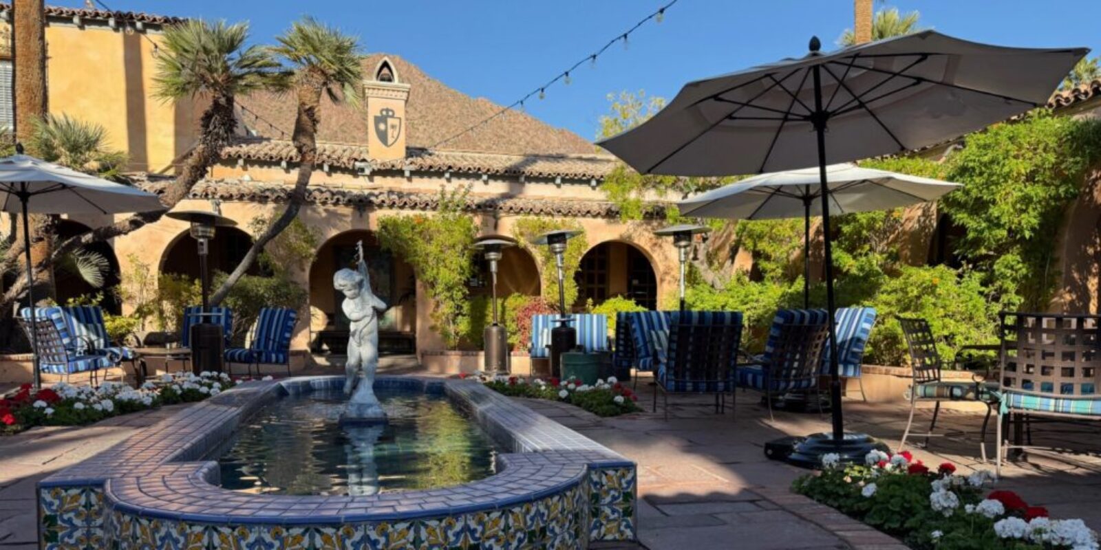 fountain with a stone statue in an outdoor courtyard flanked by several tables