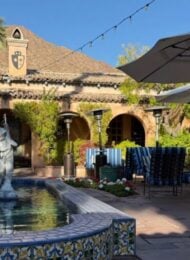 fountain with a stone statue in an outdoor courtyard flanked by several tables