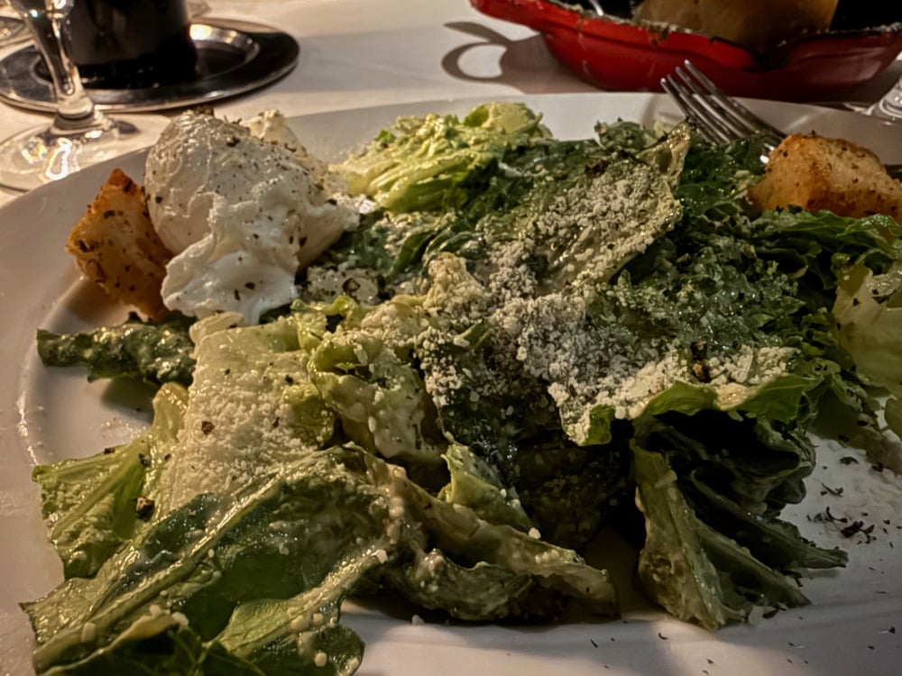 caesar salad on a white plate topped with a poached egg