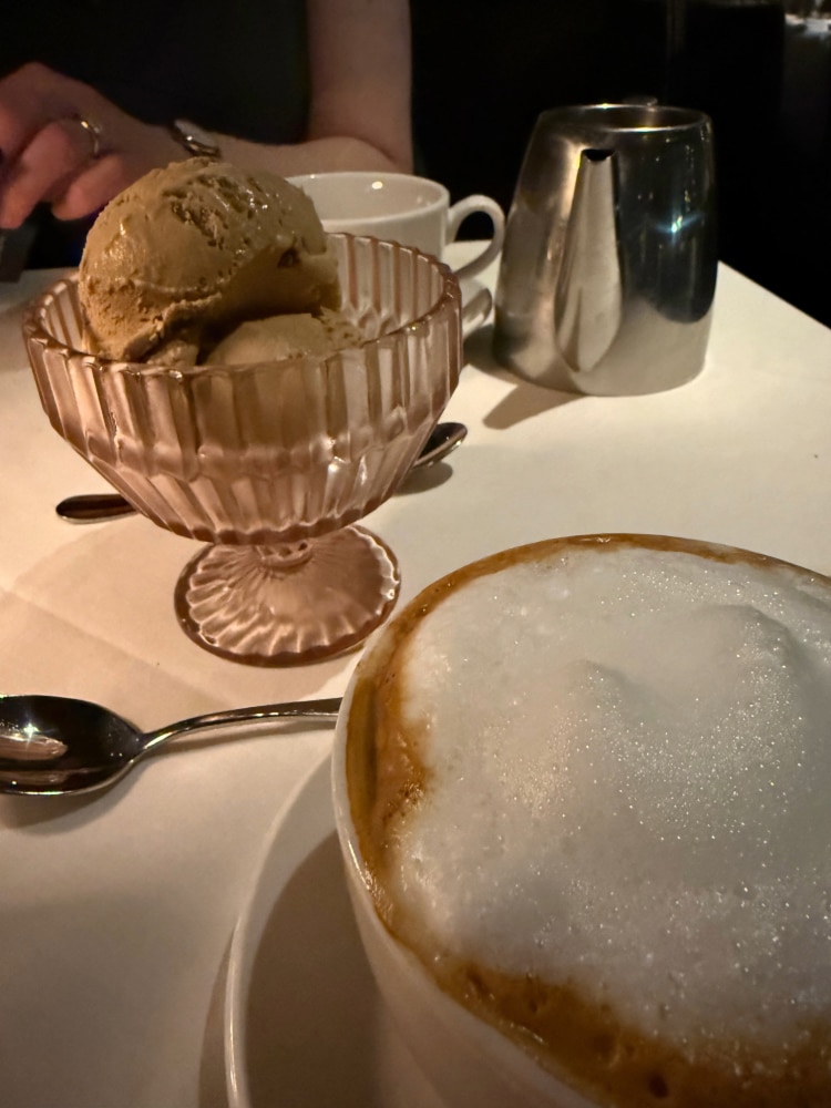 a serving of gelato in a glass dish beside a mug of cappuccino