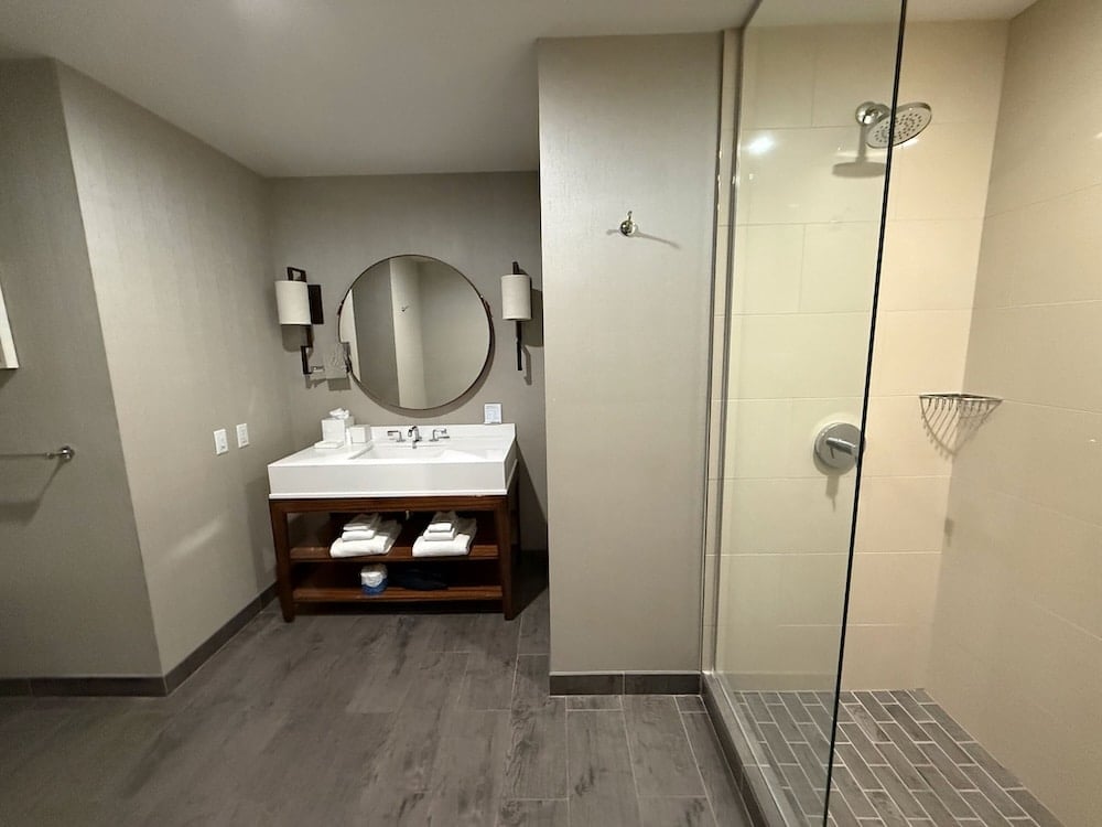 master bathroom with a sink and round mirror and a glass shower